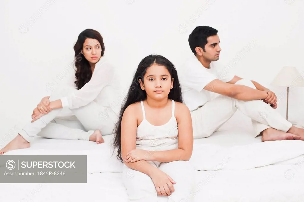 Girl sitting with her parents on the bed looking serious