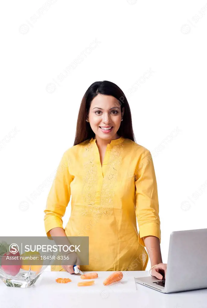 Woman using a laptop while cutting vegetables in a kitchen