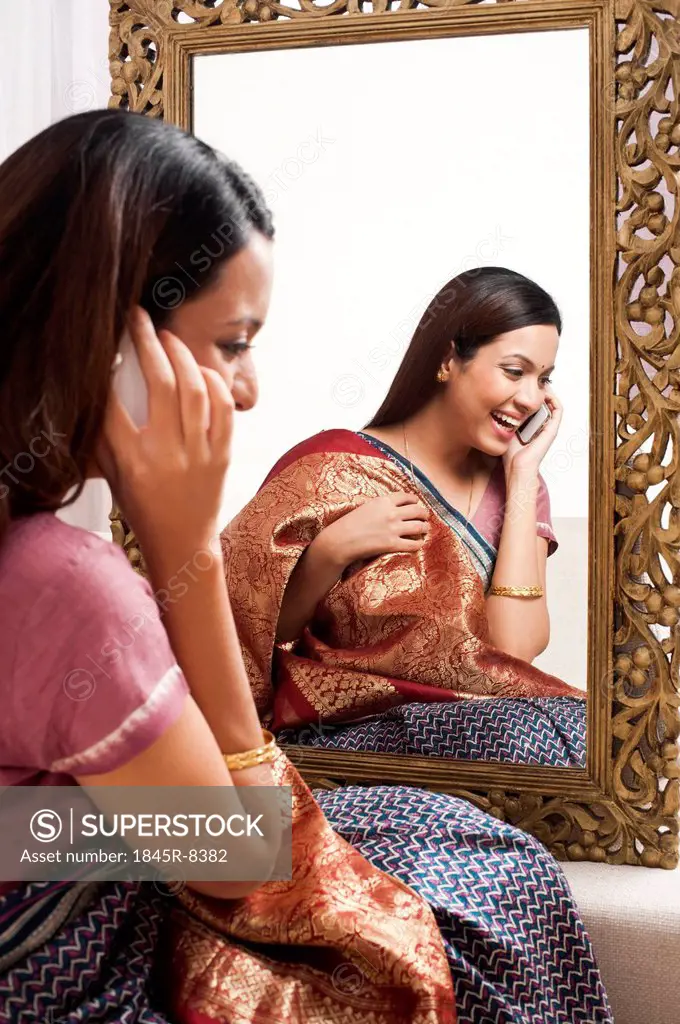 Reflection of a woman in mirror trying a sari on herself and talking on a mobile phone