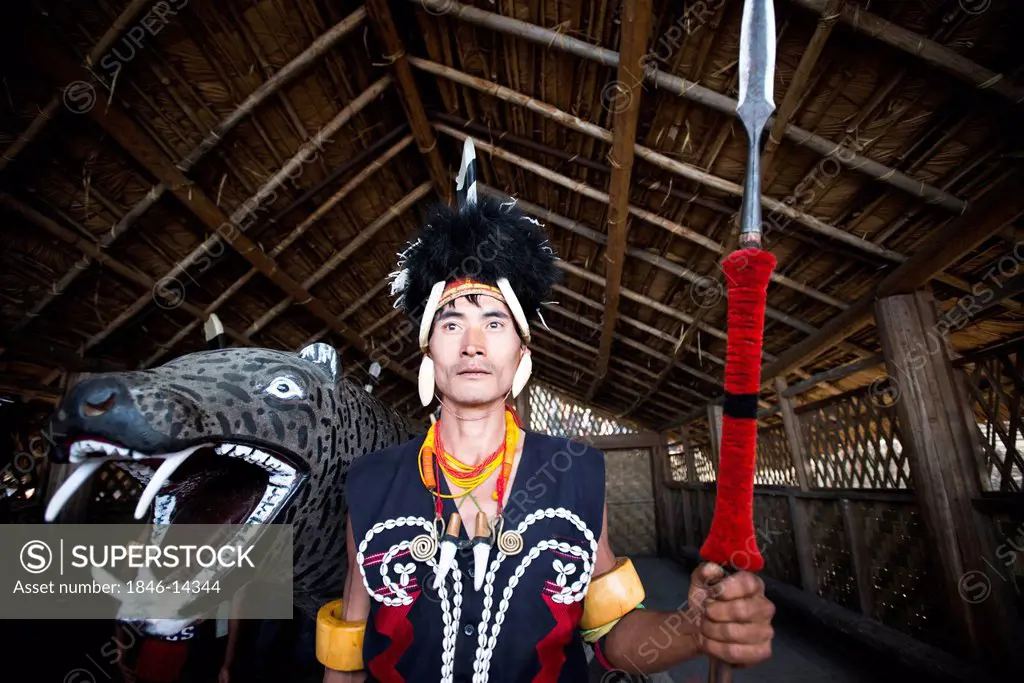 Naga tribal warrior in traditional outfit standing with a spear in a hut, Hornbill Festival, Kohima, Nagaland, India