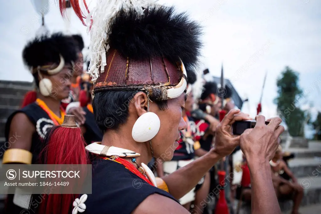 Naga tribal man in traditional outfit taking picture of an event in Hornbill Festival, Kohima, Nagaland, India