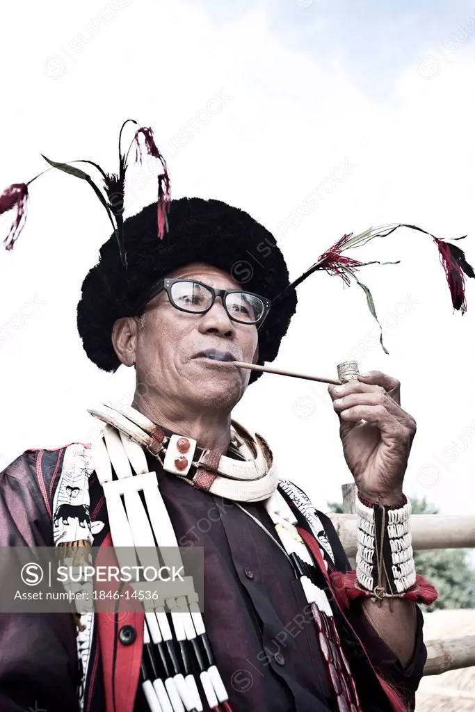 Naga tribal man in traditional outfit smoking pipe, Hornbill Festival, Kohima, Nagaland, India