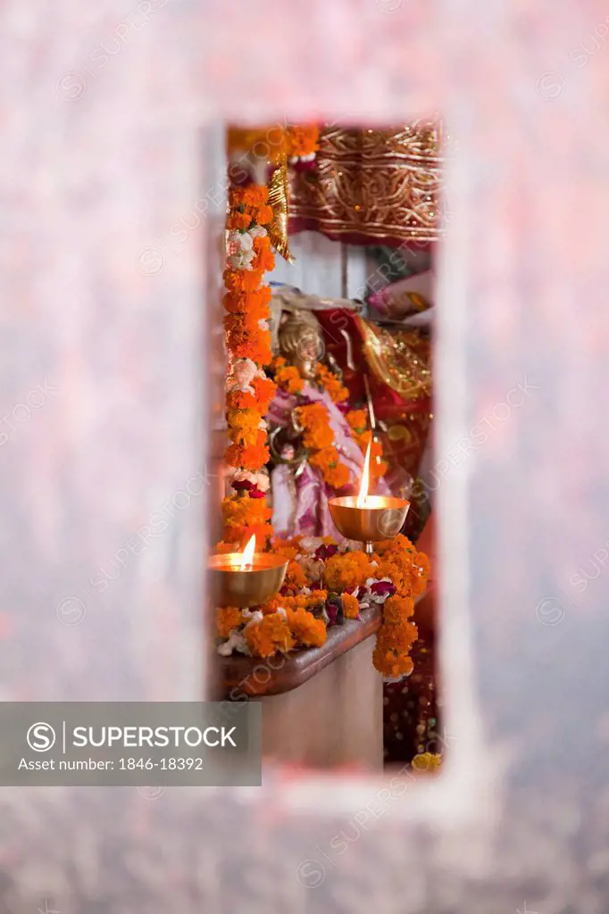 Burning oil lamps in a temple viewed through a slot in wall, Chandi Temple, Haridwar, Uttarakhand, India
