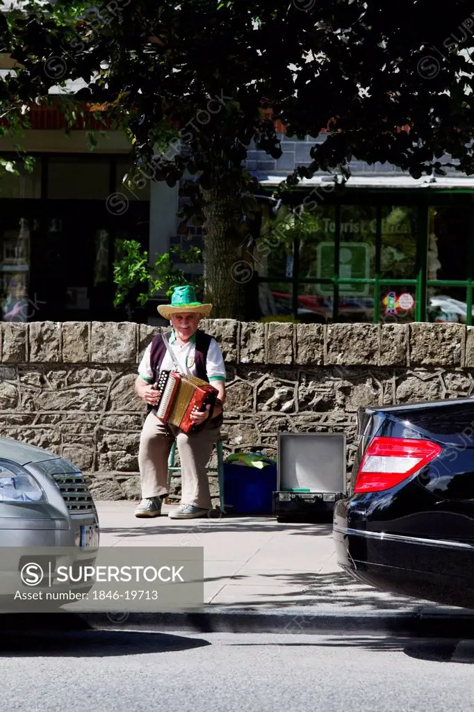 Street musician playing an accordion at the roadside, Adare, County Limerick, Republic of Ireland