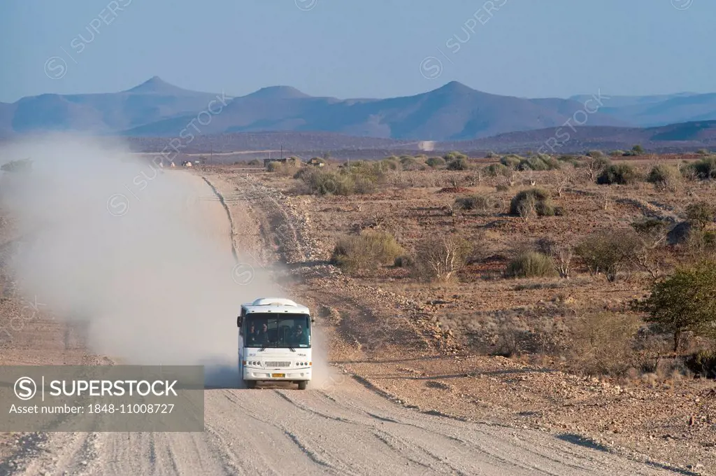 Tourist bus driving in a cloud of dust on a wide, dusty gravel road, Kunene Region, Namibia