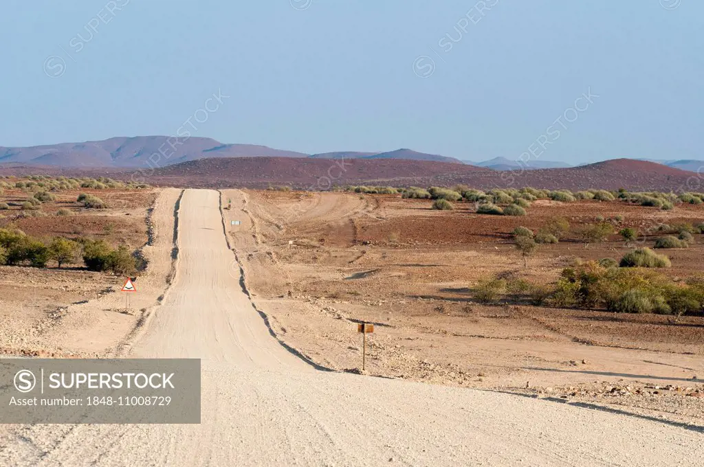 Wide, straight gravel road in dry landscape, Kunene Region, Namibia