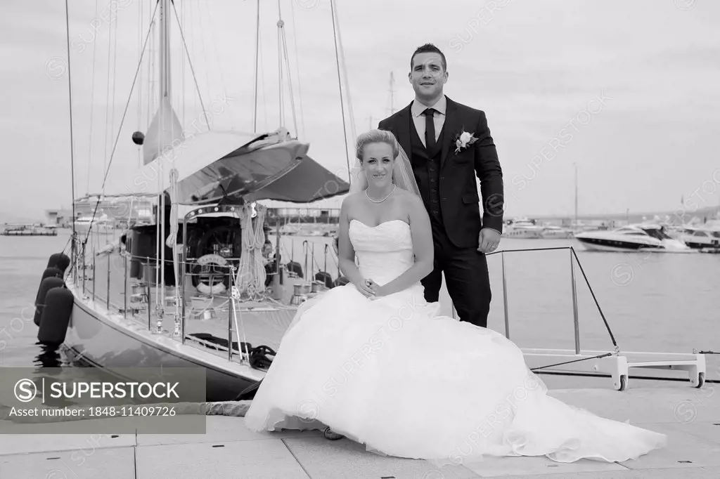 Bride and groom posing in front of a yacht in a marina
