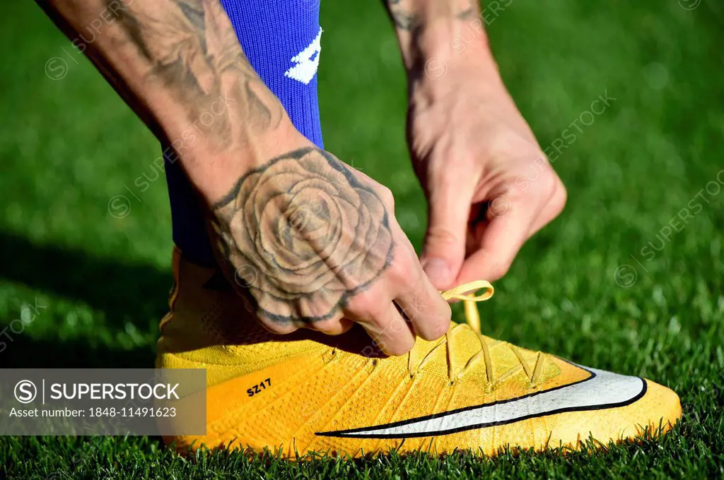 Football player tying the laces of his soccer shoes, tattoo