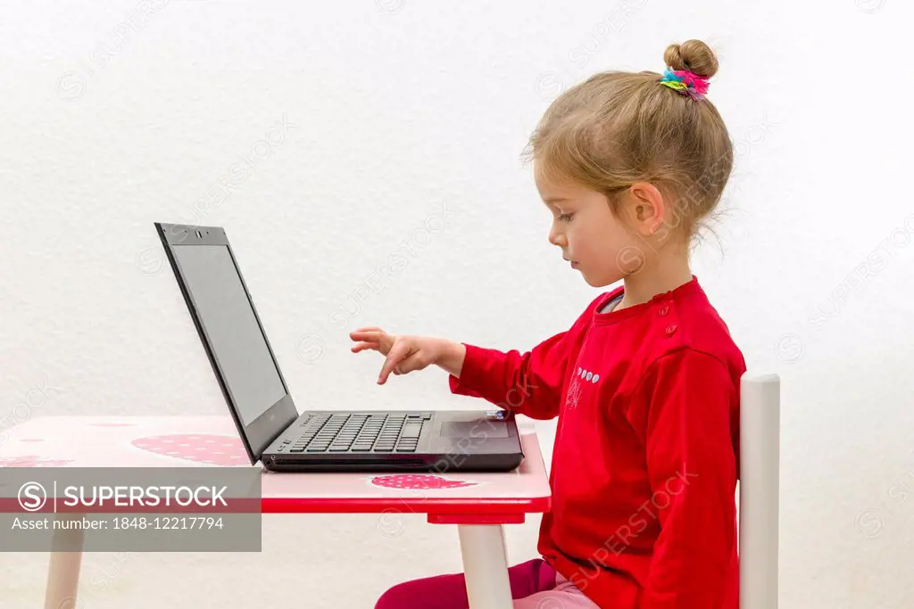 Girl, 3 years, sitting at a table, using a laptop