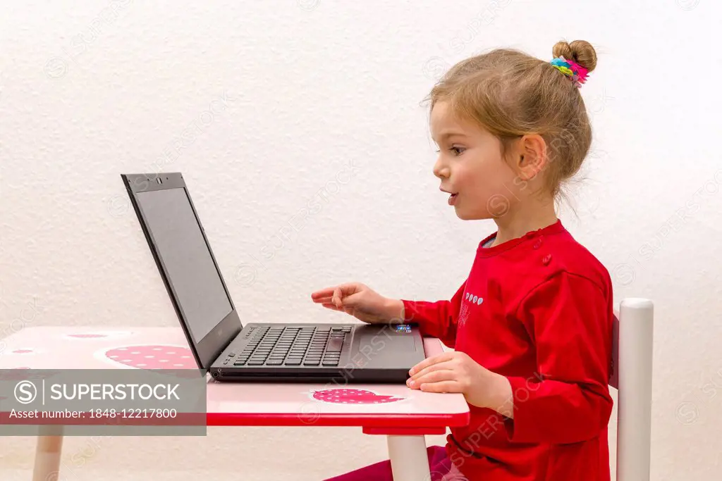 Girl, 3 years, sitting at a table, using a laptop