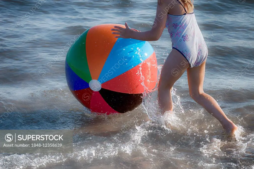Girl playing with a colourful beach ball in the sea