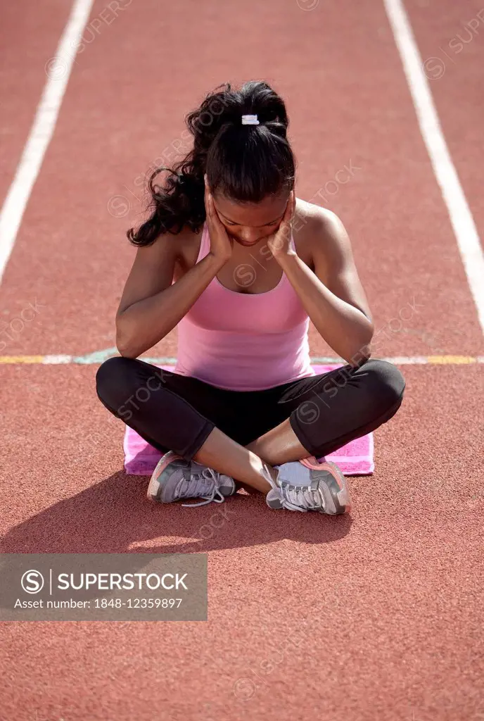 Sporty young woman, meditating, sitting on race track, getting mentally ready