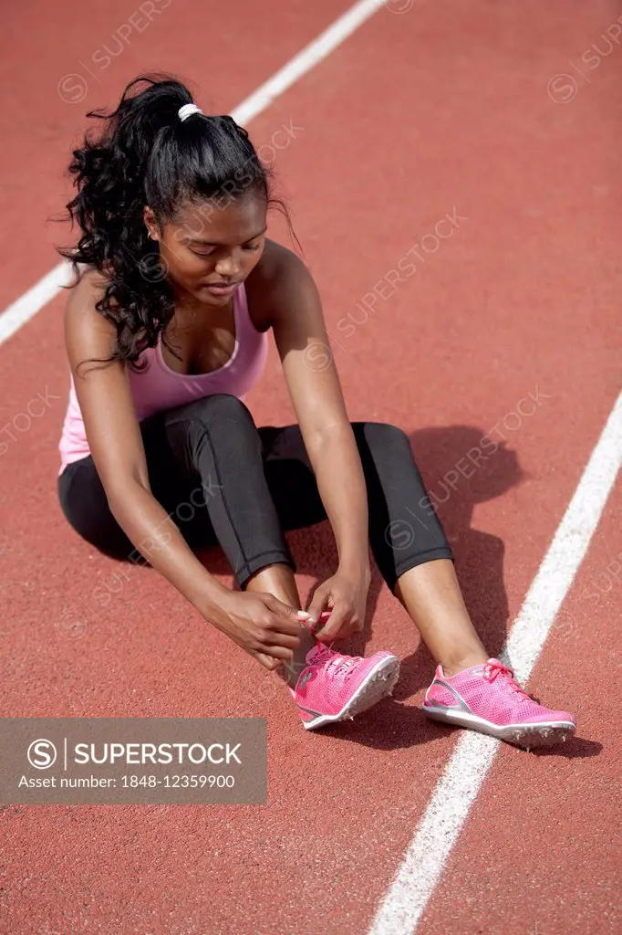Sporty young woman, sitting on race track, tightening her running shoes