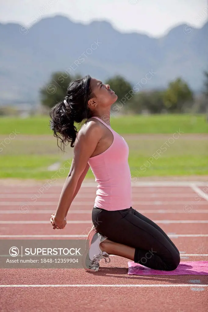 Sporty young woman on running track, stretching arms