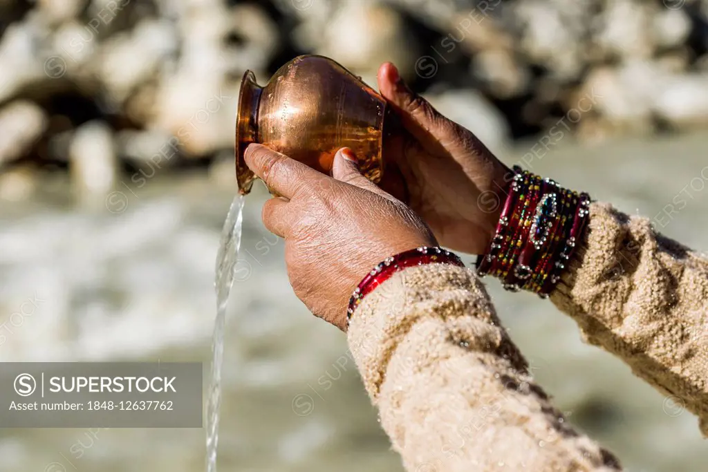 A female pilgrim praying, offering the holy water, at the banks of the river Ganges, Gangotri, Uttarakhand, India