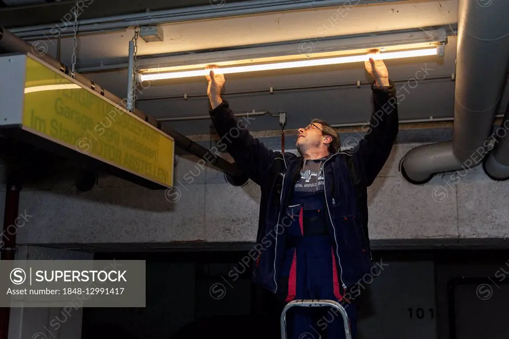 Caretaker replacing fluorescent lamp in underground garage