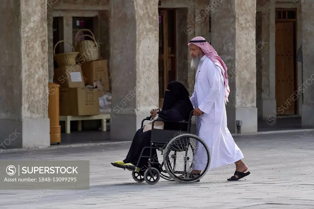 Local man pushing a veiled woman in a wheelchair, Doha, Qatar