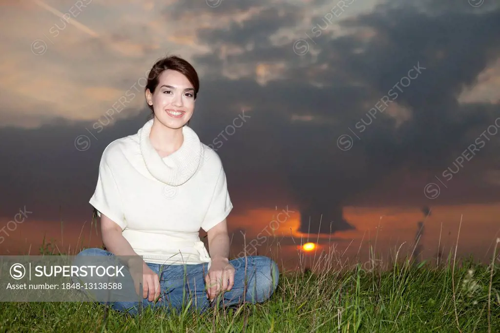 Smiling young woman sitting in a meadow, sunset