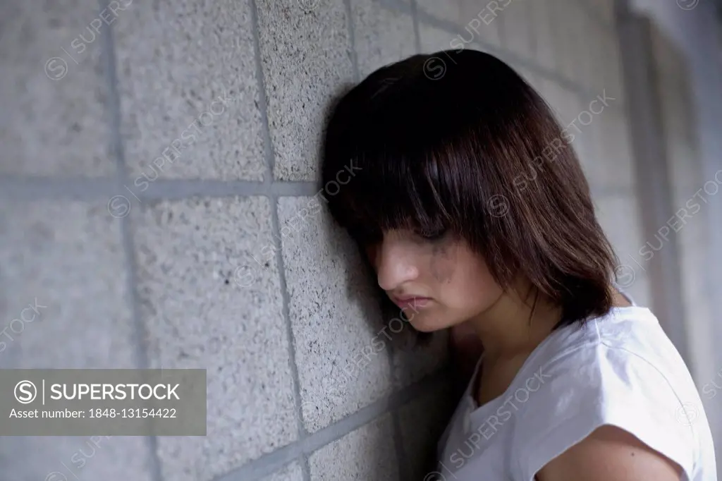 Sad young woman leaning against a wall