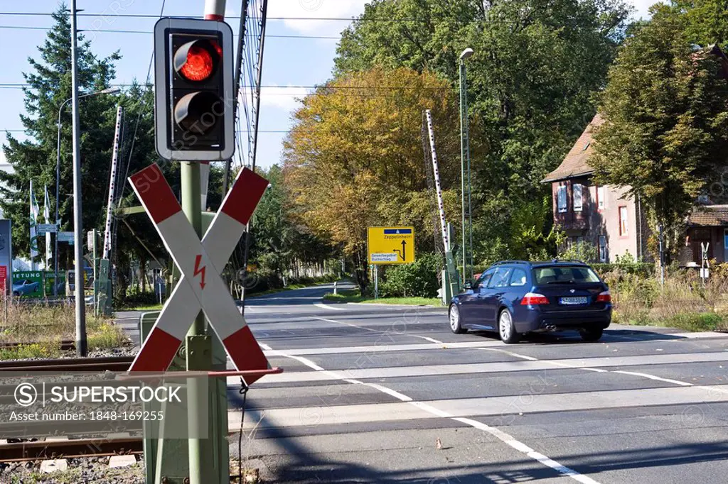 Car is driving over an railway level crossing with opened gates, with St Andrew´s Cross and red traffic light, Hessen, Germany