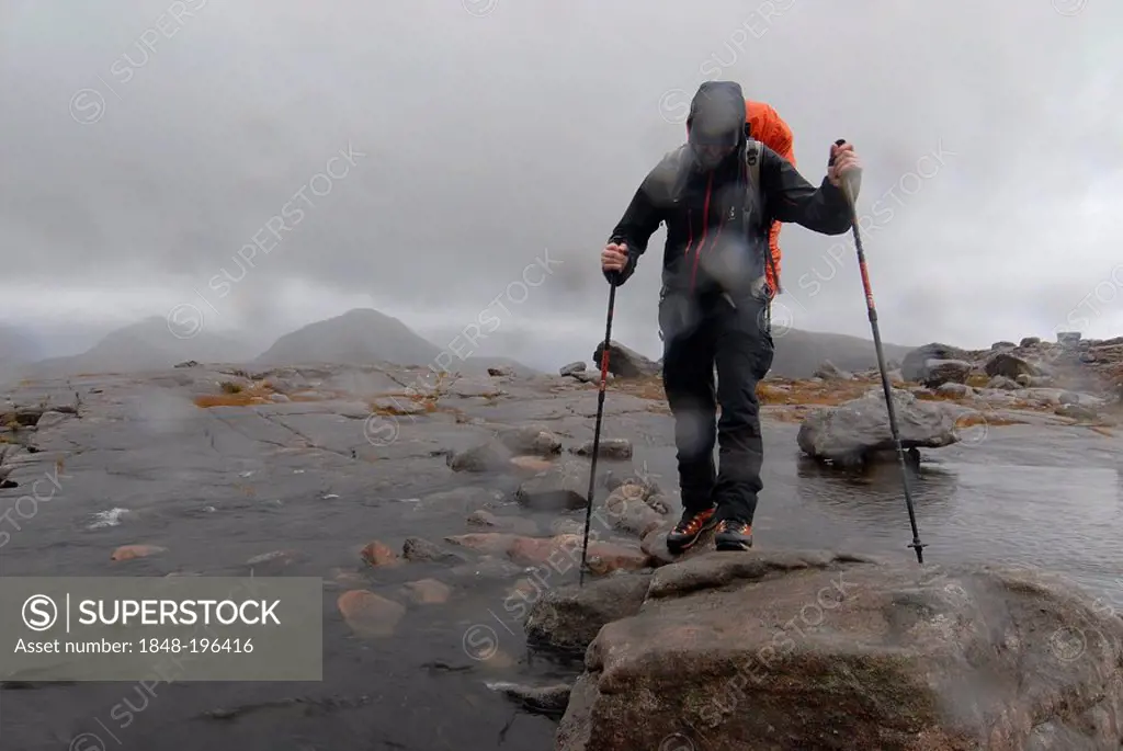 Hikerswith hiking poles and and slicker crossing a river in the Scottish rain, Scottish Highlands, Liathach, Torridon Scotland, UK, Europe