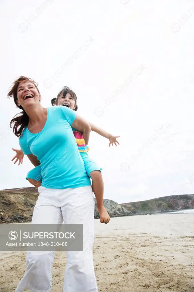 Woman carrying a girl on her back, on the beach