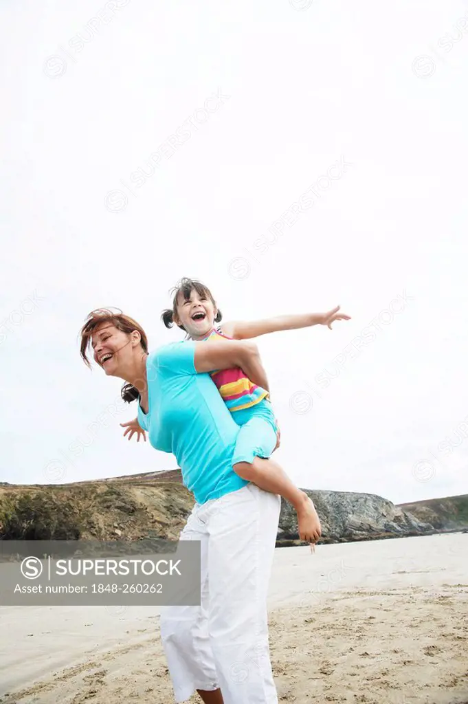 Woman carrying a girl on her back, on the beach