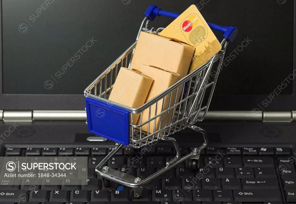 Online shopping, a shopping cart filled with parcel and a credit card standing on the keyboard of a notebook computer