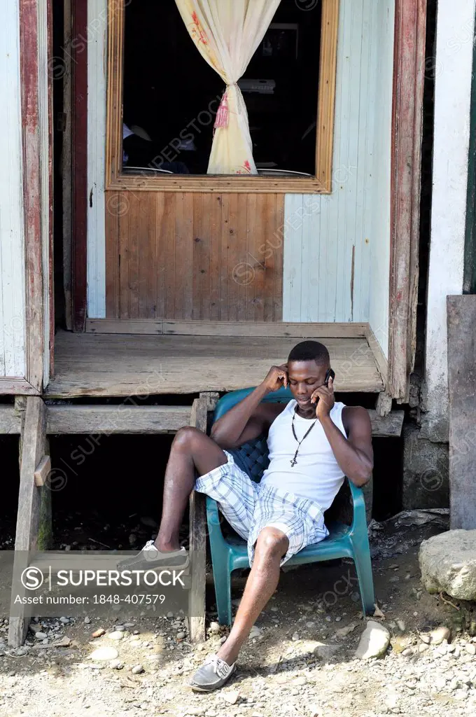 Young man on a plastic chair, Afro-Colombians, on the phone, Bajamar slum, Buenaventura, Valle del Cauca, Colombia, South America