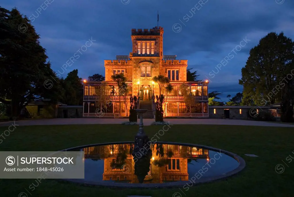 Larnach Castle on the Otago Peninsula and its reflexion in the pond of a fountain illuminated by floodlight, New Zealand