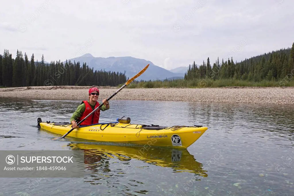 Young woman in kayak, paddling, kayaking, clear, shallow water of upper Liard River, Pelly Mountains behind, Yukon Territory, Canada
