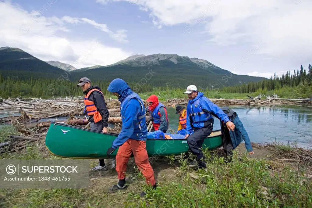 Men portaging, carrying a canoe over land, bypassing obstacle, log jam behind, upper Liard River, Yukon Territory, Canada