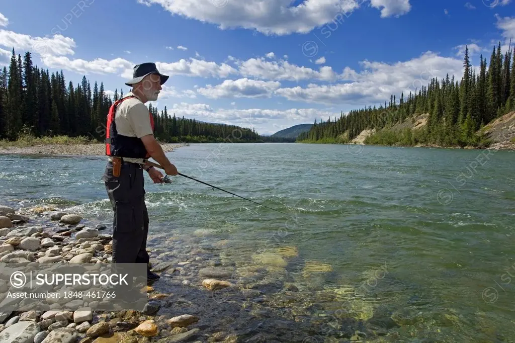 Man fishing upper Liard River, clear, shallow water, mountains behind, Yukon Territory, Canada
