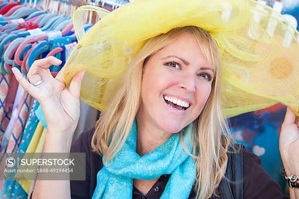 Happy blonde woman playfully modeling a big sun hat at the market