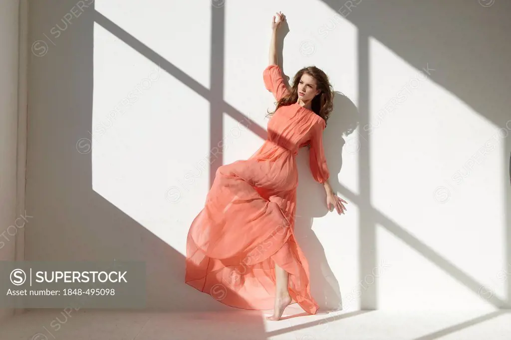 Ballet dancer wearing a red dress leaning against a wall in a dance pose