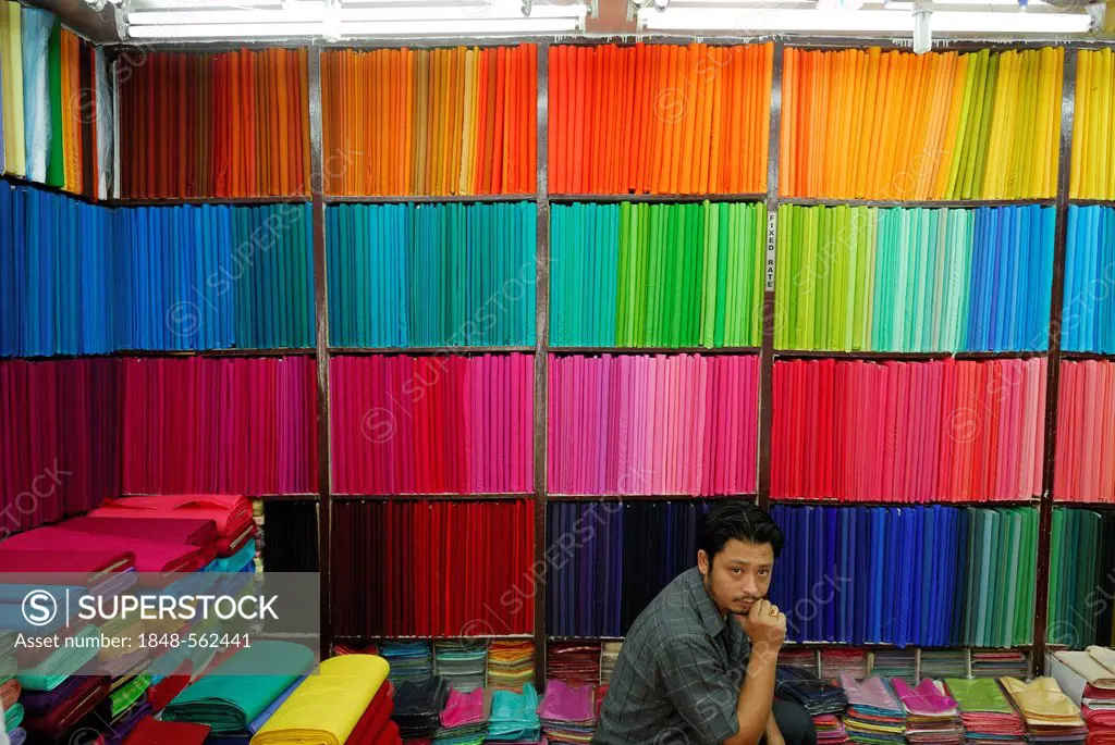 Young man in a fabric store, colourful fabrics on a shelf, rolls of fabric, Kathmandu, Nepal, Asia