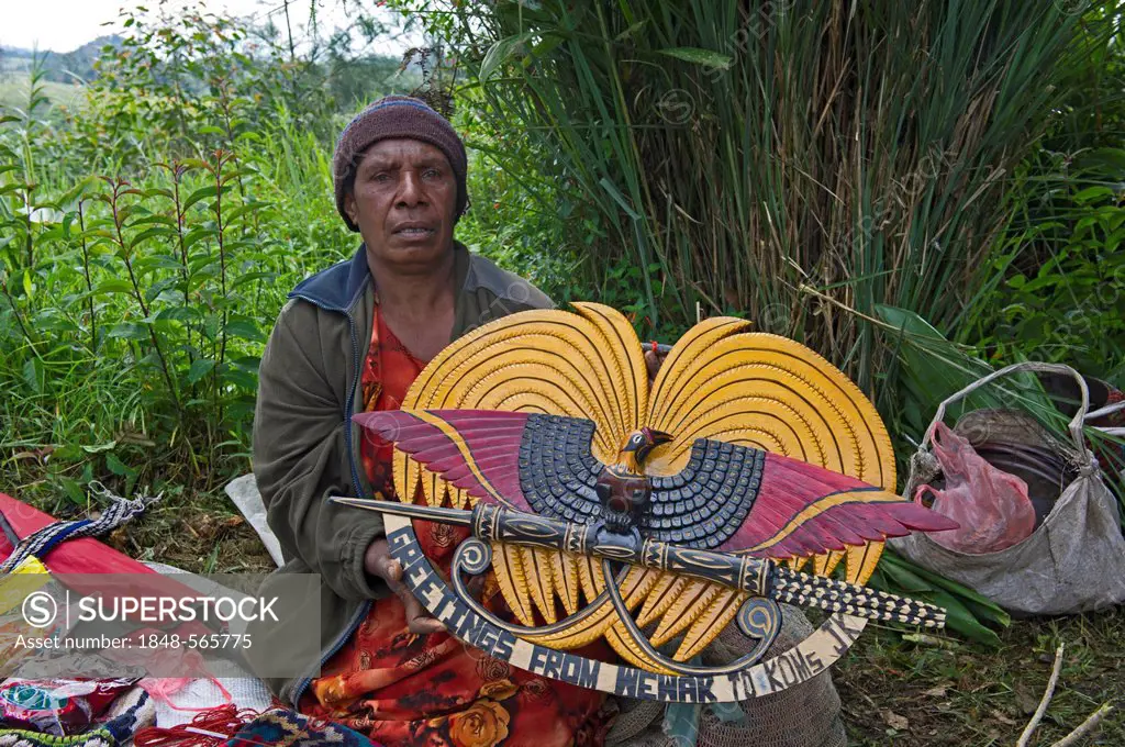 Lady selling wooden carved plaque of Papua New Guinean design of national emblem which depicts a displaying plumed bird of paradise, Paiya Show, Weste...