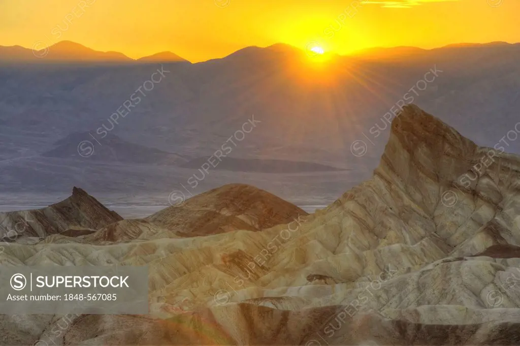 View from Zabriskie Point to Manly Beacon with eroded rocks discoloured by minerals, Panamint Range at back, sunset, Death Valley National Park, Mojav...