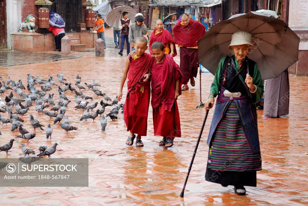 Pilgrim carrying an umbrella and monks walking around the Bodnath Stupa in the rain, Kathmandu, Nepal, Asia