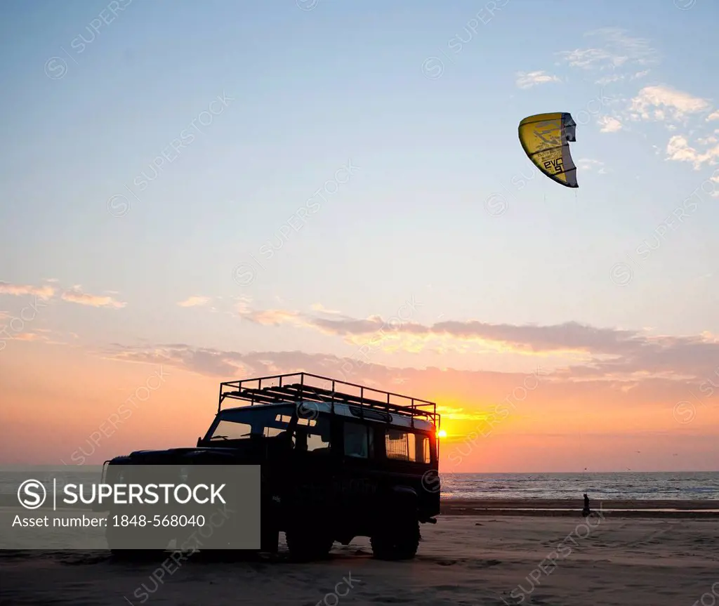 Silhouette of an off-road vehicle and a kite surfer on the beach of Egmond aan Zee at sunset, Netherlands, Europe