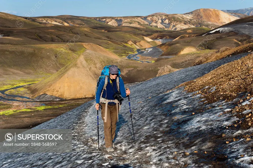 Female hiker walking on a snow field, rhyolite mountains covered with ash and snow on the Laugavegur hiking trail, Landmannalaugar Hrafntinnusker, Fja...