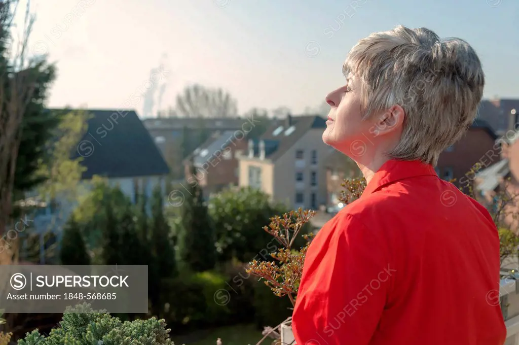 Woman wearing a red blouse standing on a balcony, enjoying the sunshine, Grevenbroich, North Rhine-Westphalia, Germany, Europe