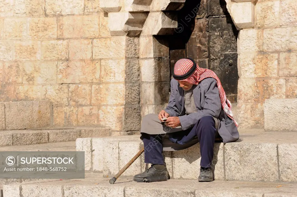Palestinian man with keffiyeh or kafiya sitting on his own on the steps of the Damascus Gate, Old City, Jerusalem, Israel, Middle East