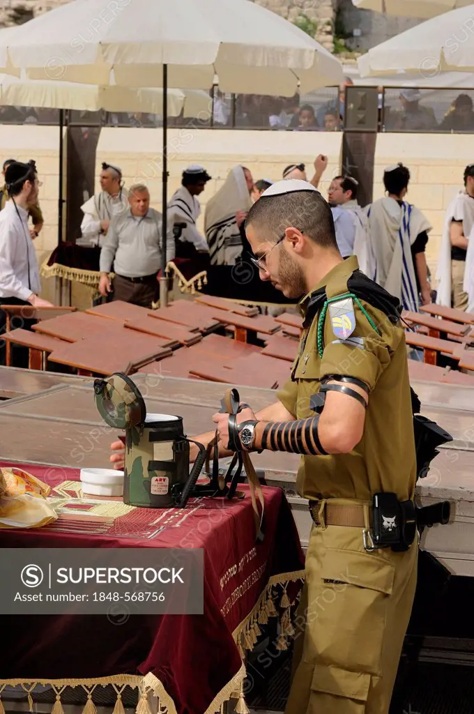 Israeli soldier getting prepared for his prayer in front of the Wailing Wall by fastening the phylacteries or tefillin, Arab quarter, historic centre,...