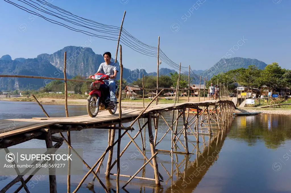 Moped rider crossing the bamboo bridge over the Nam Song River, karst mountains, Vang Vieng, Vientiane, Laos, Indochina, Asia