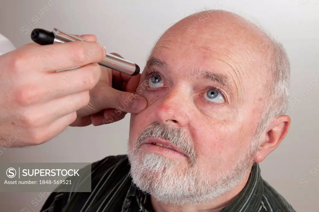 Patient, 59, at the ophthalmologist, having his eye checked with a lamp