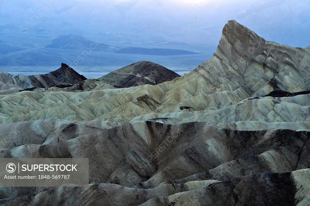 View from Zabriskie Point to Manly Beacon with eroded rocks discoloured by minerals, Panamint Range at back, dusk, Death Valley National Park, Mojave ...