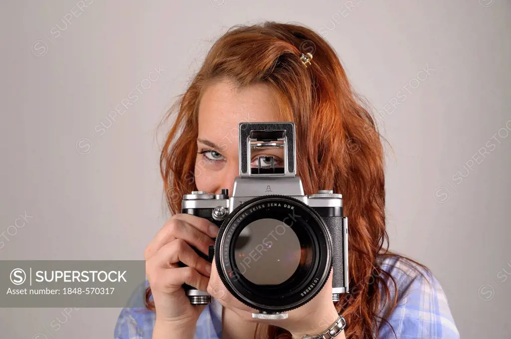 Young woman with red hair taking a photograph with an analog medium format camera Pentacon Six
