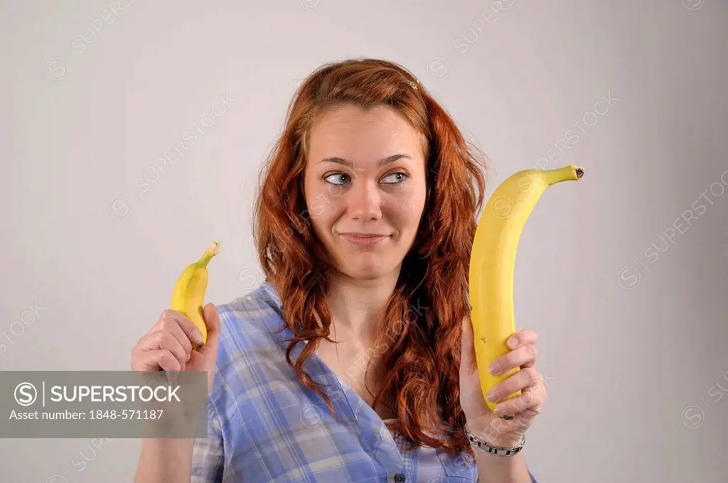Young woman with red hair comparing a very large and a very small banana in her hands