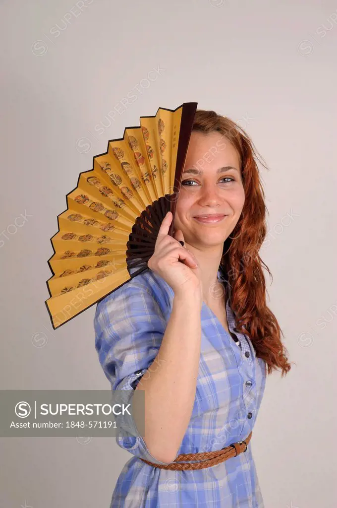 Young woman with red hair holding a fan in front in front of her face
